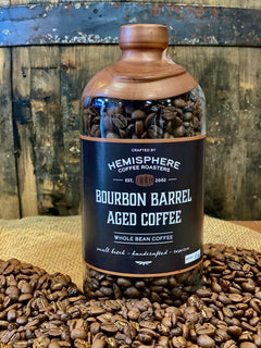Large barrel-aged coffee bottle on a bed of roasted beans — Hemisphere Bourbon Barrel-Aged Coffee, 11 oz Bottle