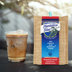 Plantation Blue 8 oz dark ground Jamaica Blue Mountain coffee package next to a glass of iced milk coffee