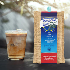 Plantation Blue 12 oz dark ground Jamaica Blue Mountain coffee package next to a glass of iced milk coffee