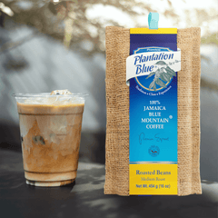 Plantation Blue 16 oz medium whole-bean Jamaica Blue Mountain coffee package next to a glass of iced milk coffee
