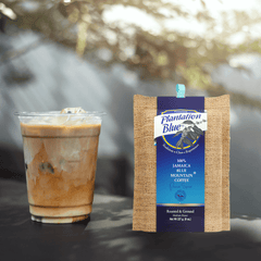 Plantation Blue 8 oz medium ground Jamaica Blue Mountain coffee package next to a glass of iced milk coffee