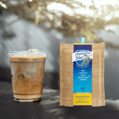 Plantation Blue 8 oz medium whole-bean Jamaica Blue Mountain coffee package next to a glass of iced milk coffee