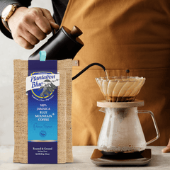 Plantation Blue 16 oz medium ground Jamaica Blue Mountain coffee beside a hand pouring from a black kettle into a filter brewer
