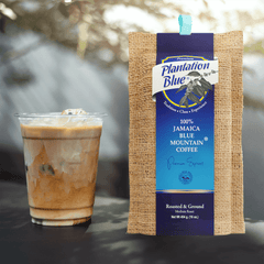 Plantation Blue 16 oz medium ground Jamaica Blue Mountain coffee package next to a glass of iced milk coffee