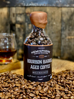 Small barrel-aged coffee bottle with a wooden stopper among roasted beans — Hemisphere Bourbon Barrel-Aged Coffee, 5.5 oz Bottle