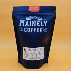 Blue Mainely Nine Mile coffee pouch against a mustard-yellow background