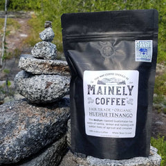 Black Mattagamon coffee bag standing beside stacked gray stones