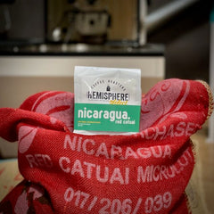Red Catuai bag centered between the raised sides of a red sack — Hemisphere Nicaragua Red Catuai Light Roast, 10 oz