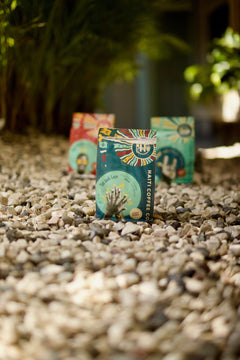 Front of a teal Tèt āndi Laye coffee bag on gravel in a shaded outdoor setting