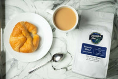 White Bespoke blend pouch beside a croissant, spoon and coffee on pale cloth