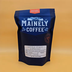 Blue Mainely Little Italy coffee bag against a mustard-colored background
