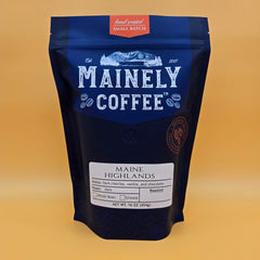Mainely Maine Highlands coffee in a blue pouch against a gold background