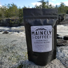 Black Cribworks coffee pouch standing on a rocky riverbank
