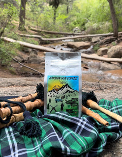 Highlander Grog coffee bag beside bagpipes and tartan fabric near a woodland stream
