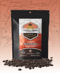 Crossed Sabers Jody’s Blend Swiss Water Decaf Coffee bag with scattered beans against a rust map backdrop