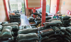 Stacks of dark coffee sacks filling a warehouse — Tiny Footprint Peru Lima Cafe Medium Roast Coffee