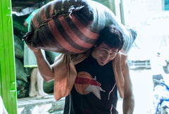 Worker carrying a large coffee sack over one shoulder — Tiny Footprint Peru Lima Cafe Medium Roast Coffee
