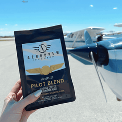 Hand holding Pilot Blend coffee near a small aircraft